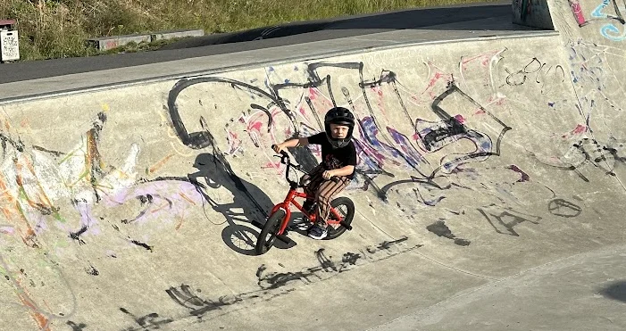 Child in a helmet on a small red BMX in a skatepark bowl