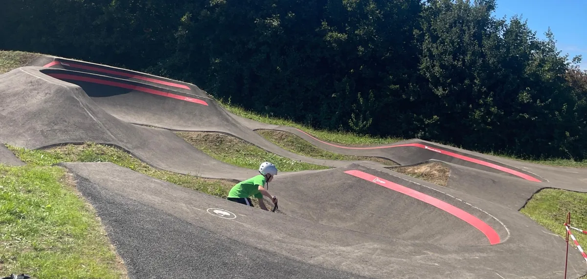 Asphaltierter Pumptrack mit Wellen und überhöhten Kurven, ein Fahrer ist auf der Strecke unterwegs