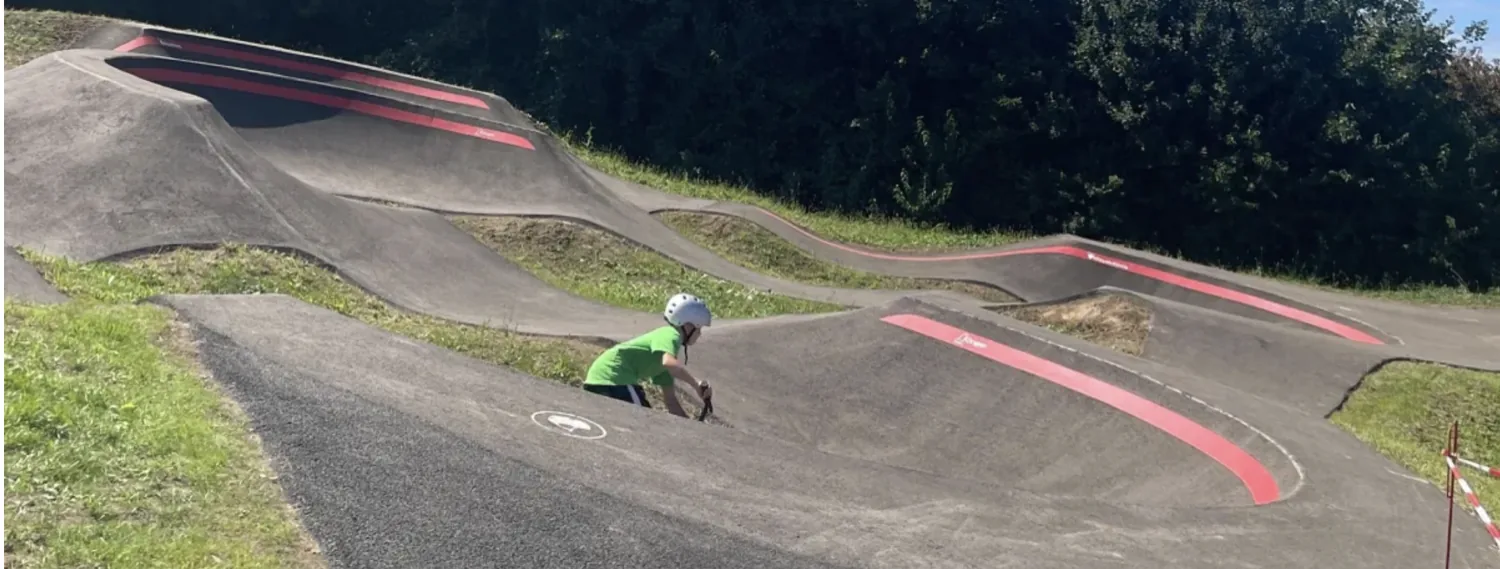 Asphalt pumptrack with rollers and banked corners, a rider out on the track